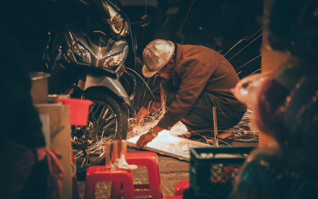 Artisan welding in a workshop, creating sparks beside a motorcycle, showcasing craftsmanship.